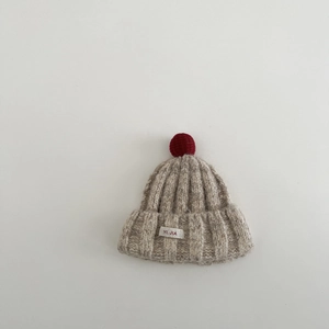 Detail der beigen Kinder-Strickmütze mit rotem Bommel und aufgenähtem YI. JIA Stoffetikett