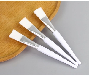 Detailed view of three white facial mask brushes with crystal clear handles on a wooden tray