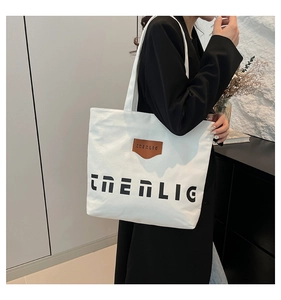Detail of white canvas tote bag featuring brown leather logo patch and black lettering