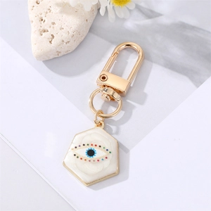 Detail of a gold hexagon keychain with a white enamel evil eye charm and lobster clasp