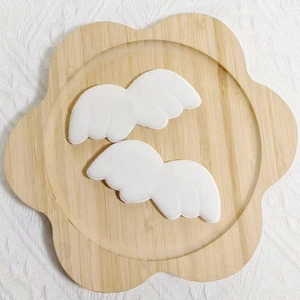 Détail d'ailes en peluche blanches pour poupées sur un plateau fleuri en bois