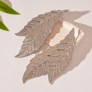 Macro shot of silver leaf-shaped earrings on stone base showing fine texture and relief