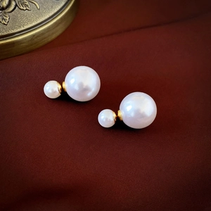 Detail of white double faux pearl earrings with golden metal stems on brown fabric