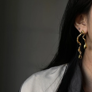 Close-up of golden irregular wavy drop earrings with a polished liquid metal finish on model
