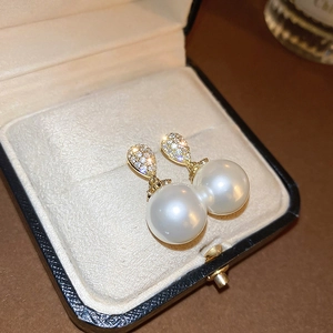 Macro detail of gold plated pearl earrings with sparkling zircon accents in a gift box