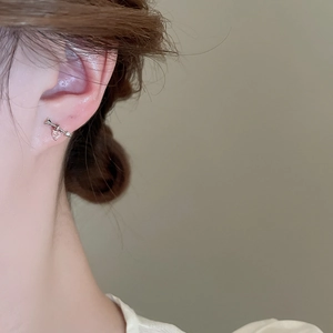 Detail of silver stud earrings featuring pink heart zircon and arrow design on ear