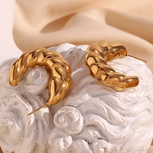 Macro view of gold plated croissant dome hoop earrings on a textured white stone base