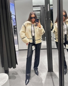 Detail of cream faux shearling biker jacket with black trim and leather trousers