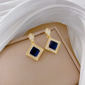 Macro detail of gold earring with square blue gemstone and pavé diamond border