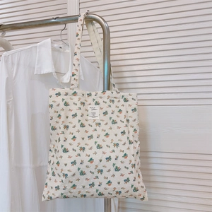 Detail of floral canvas tote bag hanging on rack featuring botanical print and fabric label