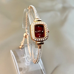Macro detail of rose gold watch with red rectangular dial and sparkling crystal accents