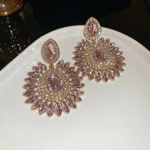 Macro detail of pink crystal flower earrings on a white tray with gold finish