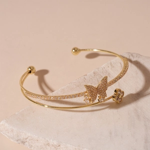 Detail of gold double-layer bangle with zircon butterfly and clover on a stone base