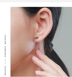 Close-up of a silver dinosaur stud earring with purple zircon worn on a model ear