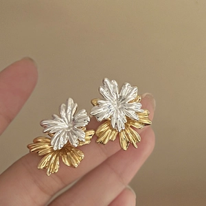 Detail of two-tone flower earrings held in hand to show the size and metallic texture