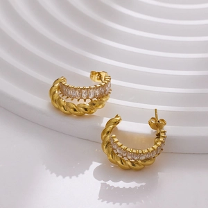 Close-up of golden C-shaped hoop earrings with twisted rope and baguette-cut CZ inlay