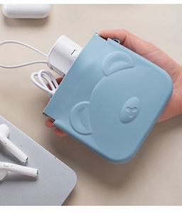 Hand holding a blue bear silicone pouch storing a white USB charger and data cable