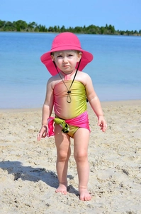Detailansicht eines Kleinkindes mit einem rosa atmungsaktiven Sonnenhut am Strand