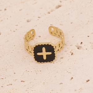 Détail d'une bague dorée réglable avec croix en émail noir et anneau texturé