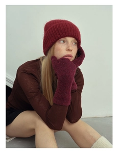 Detail view of deep red knitted wool gloves and matching hat on a female model