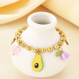 Detail of beaded gold bracelet with enamel strawberry and avocado charms on a white vase