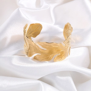 Detail of golden hollow leaf cuff bracelet with fine textures on white silk