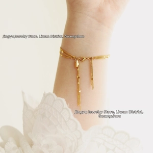 Detail view of a multi-layer gold tassel bracelet with heart pendant on a female wrist
