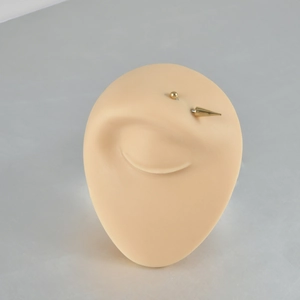 Detail view of a golden stainless steel curved eyebrow piercing on a silicone model ear