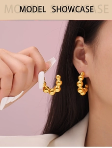 Close-up of gold C-shaped beaded stud earrings on model with sleek metal finish