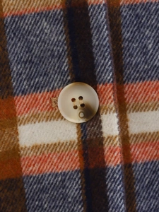 Dettaglio macro della trama in flanella a quadri con bottone beige sul cappotto scozzese