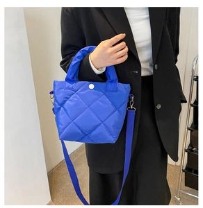 Detail of royal blue quilted handbag with matching strap against a dark blazer background