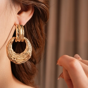 Close-up of large gold textured hoop earrings with wavy design on a female model