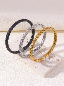 Detailed view of three braided stainless steel wire cuff bracelets in gold, silver, and black