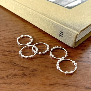 Set of five minimalist silver bead rings arranged on a rustic wooden surface with a book