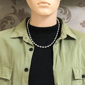 Silver bead chain necklace worn by a model over a black turtleneck and green shirt