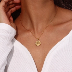 Detail of gold necklace with zircon-encrusted sunburst pendant on a knit sweater