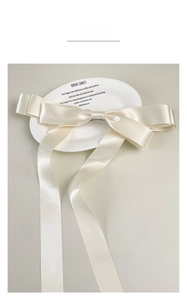 Detail of cream satin bow hair clip with long ribbons on a decorative ceramic plate