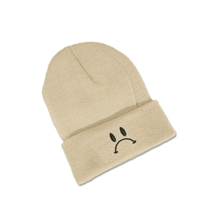 Détail du bonnet en maille beige montrant la broderie emoji triste et la texture épaisse