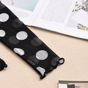 Detail eines schwarzen Mesh-Langarmshirts mit weißen Punkten auf beigem Hintergrund