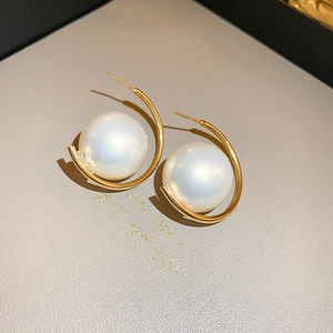 Detailed view of large white pearl nestled in a gold C-shaped metal earring setting