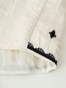 Close-up of linen-cotton fabric with black geometric embroidery on an ivory vest top