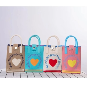Detail of four colorful knitted mini bags with heart patterns and embroidery on grid fabric