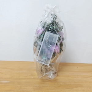 Detailed view of mini Christmas tree with purple baubles and burlap base in plastic packaging