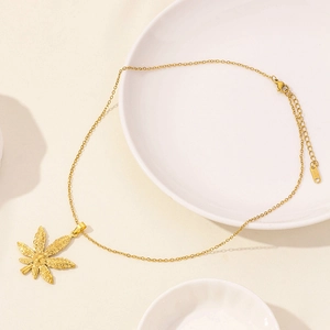 Minimalist gold stainless steel necklace with maple leaf pendant on white ceramic plate