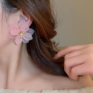 Detail shot of a pink flower petal earring with a pearl center on a female model