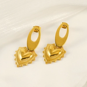 Détail macro de boucles d'oreilles cœur dorées avec texture soleil sur marbre blanc