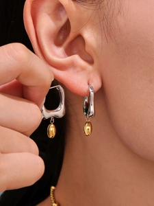 Detail of silver wavy earrings with gold bean pendants worn and held for close-up view