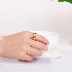 Detail of a gold X-shaped ring with pave zircons worn by a model in a minimalist setting