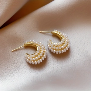 Detailed close-up of C-shaped gold hoop earrings with white pearls on beige silk fabric