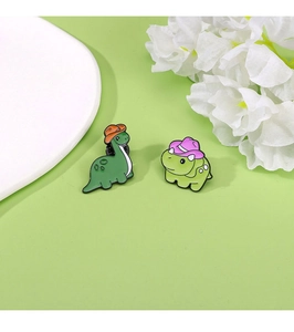 Close-up of two cute green dinosaur enamel pins with colorful hats for bag decoration